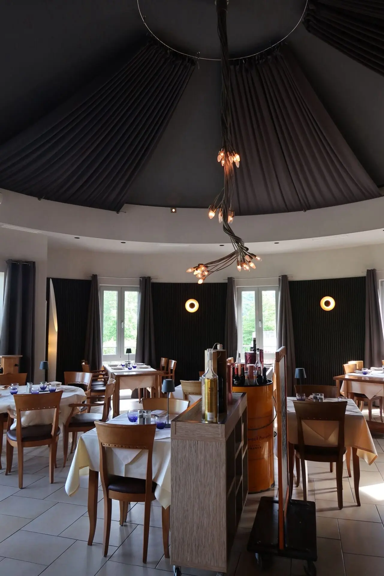 Innenansicht eines Restaurants mit runden Tischen und einer modernen Deckenleuchte.